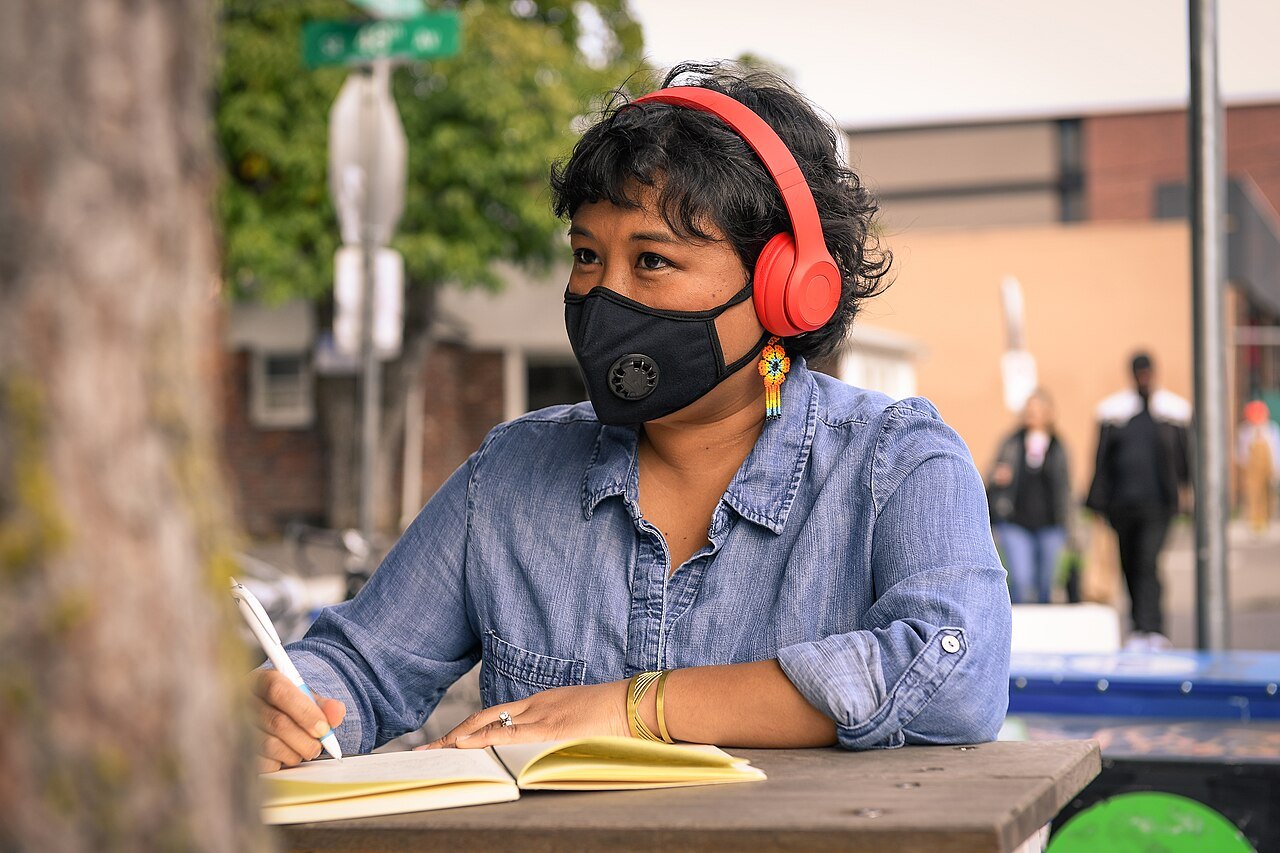 A person writing in a notebook while wearing headphones.