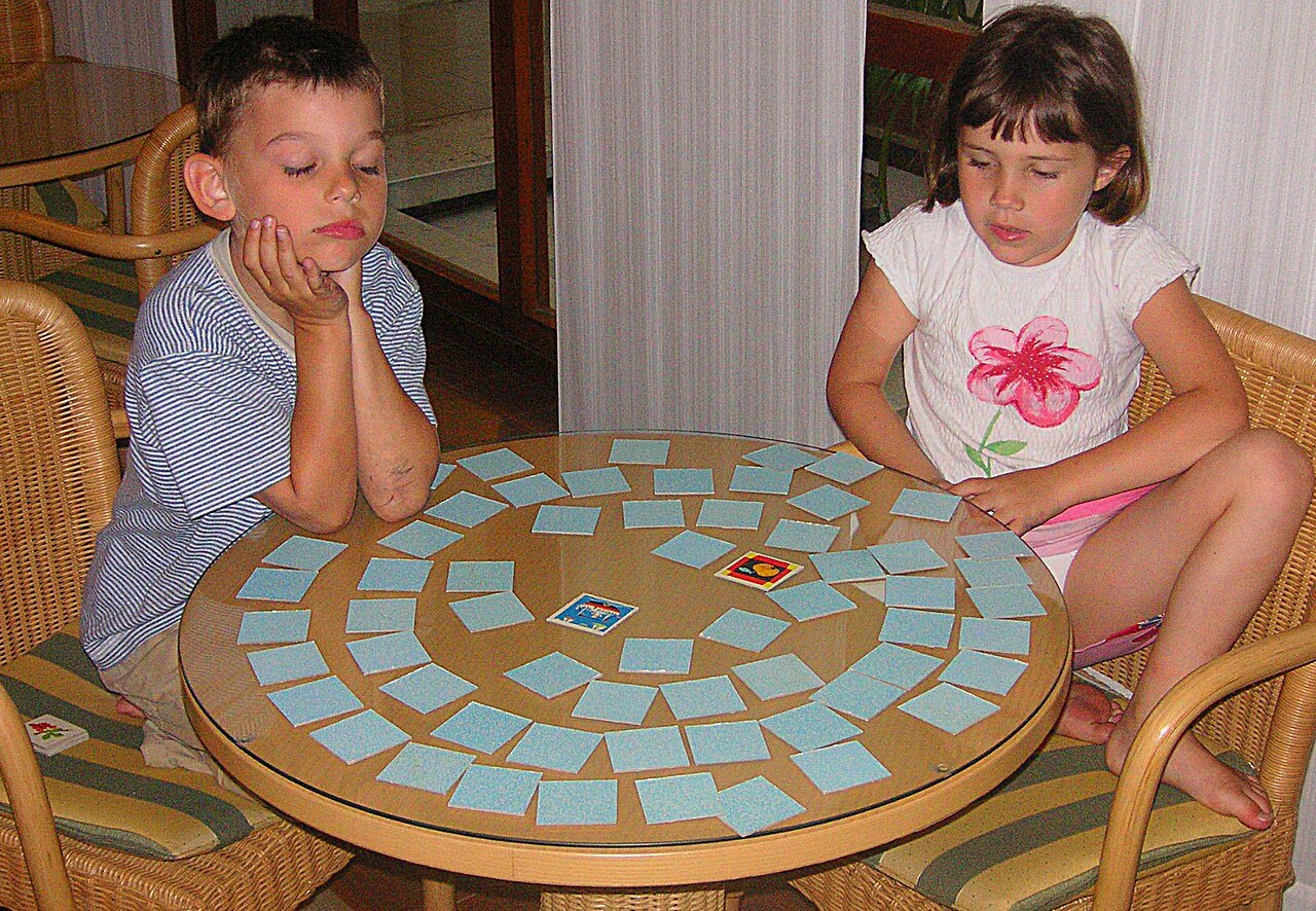 Two children playing a matching game with face-up and face-down cards.