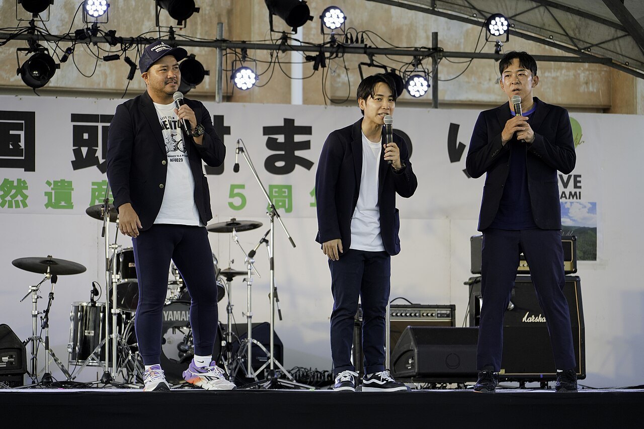 Comedy trio with handheld microphones on stage.