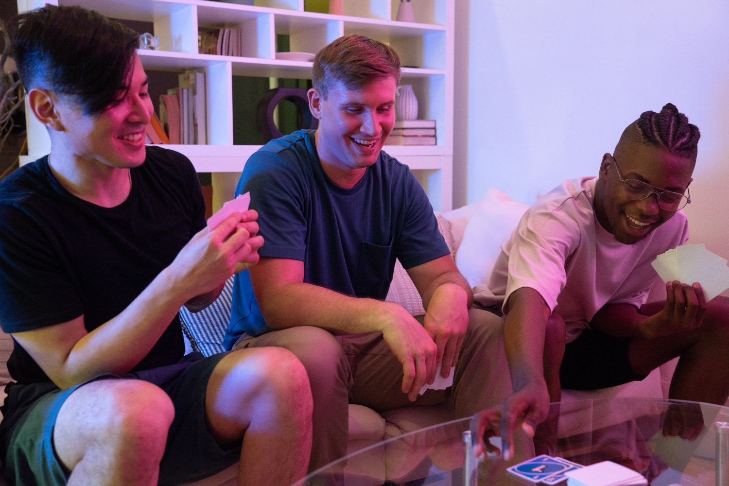 Three people play cards on a sofa.
